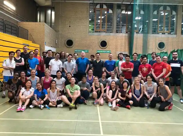 A group of badminton players posing with their rackets on an indoor court.