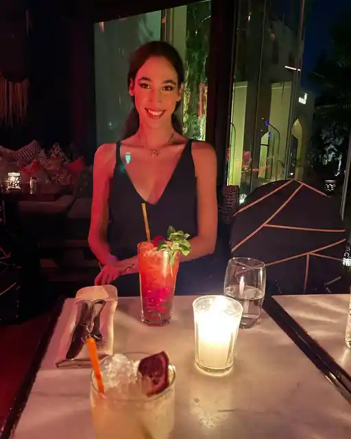 A woman smiling at a candlelit restaurant table with colourful drinks.