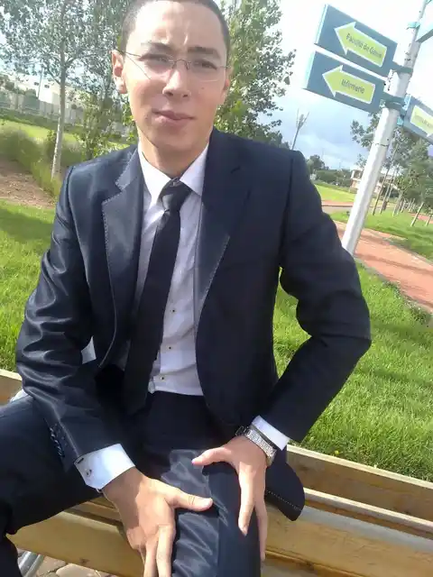 A person wearing a suit seated outdoors beside campus signposts.