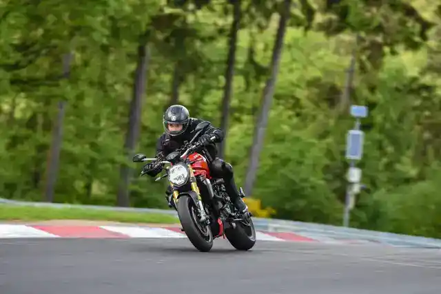 A rider leaning into a turn on a red motorcycle at a circuit.