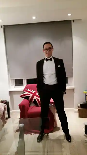 A person wearing a tuxedo and bow tie standing in a living room.